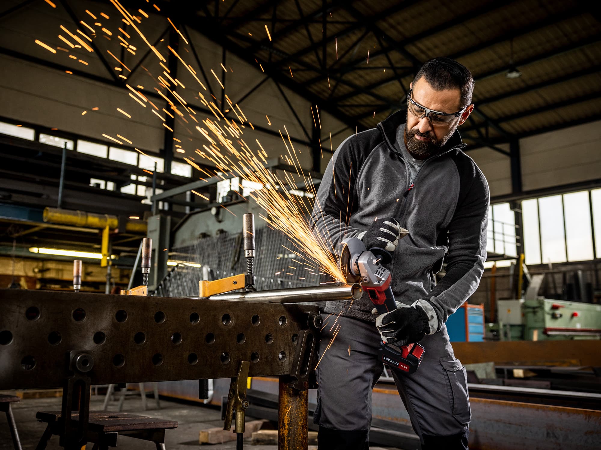 Ein Handwerker trennt ein Metallrohr mit einem FLEX Akku-Winkelschleifer.