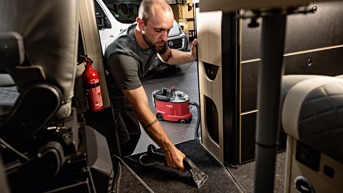 Ein Fahrzeugaufbereiter reinigt den Teppichboden eines Wohnmobils mit dem FLEX Akku-Sprühextraktionssauger.
