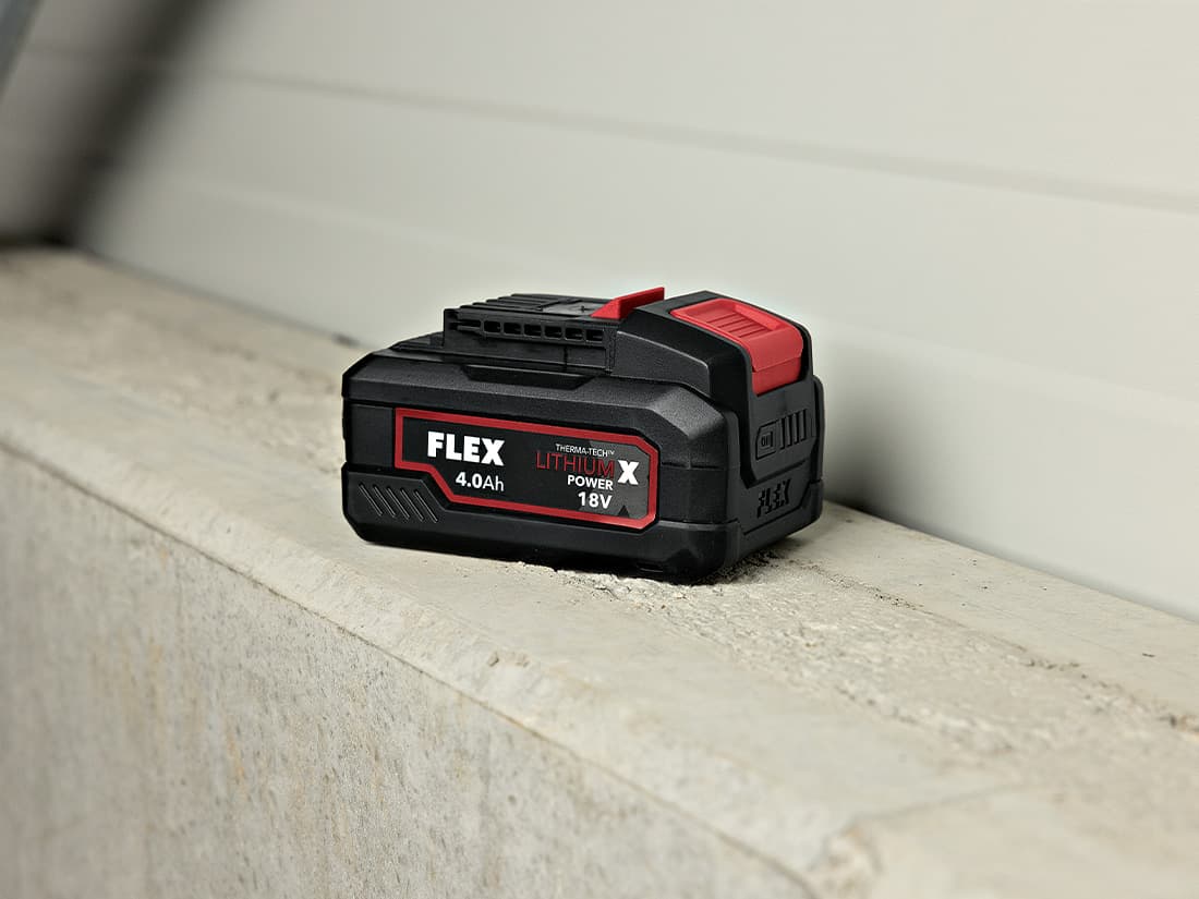 FLEX 18 V 4 Ah-batteri på en betongyta med ett +-tecken bredvid