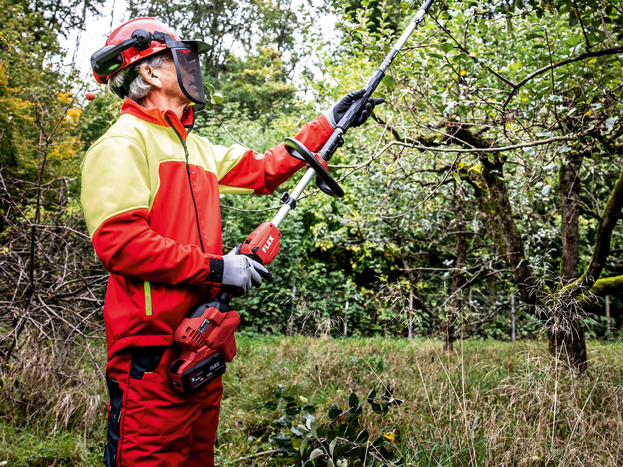 FLEX cordless base drive with pole pruner attachment in use for cutting branches.