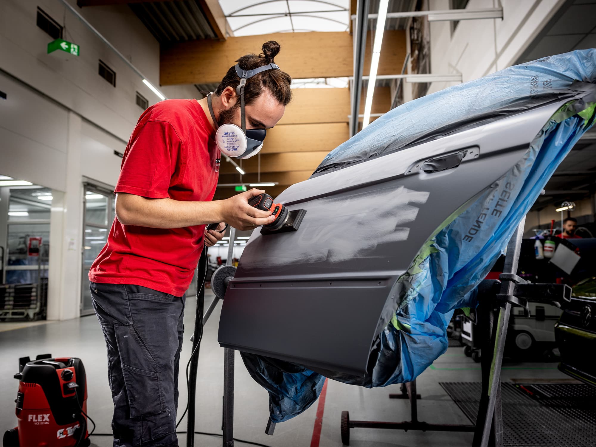 Un mecánico de carrocería lija la pintura de la puerta de un coche con la lijadora orbital de FLEX