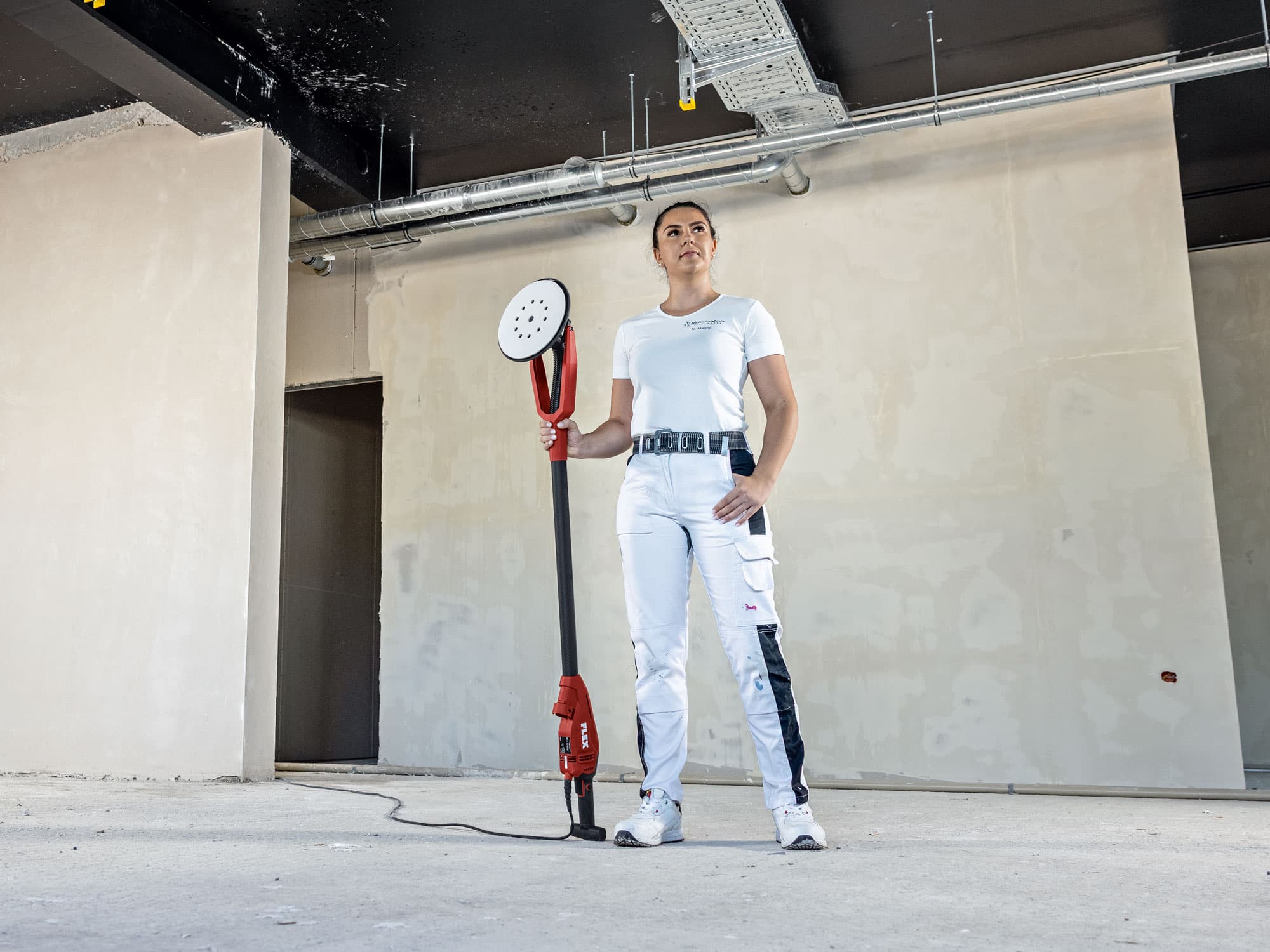 Malermeisterin Nina steht selbstbewusst auf der Baustelle und hält die neue FLEX GE 6 X mit exzentrischem Antrieb – einen Wand- und Deckenschleifer – in der Hand.