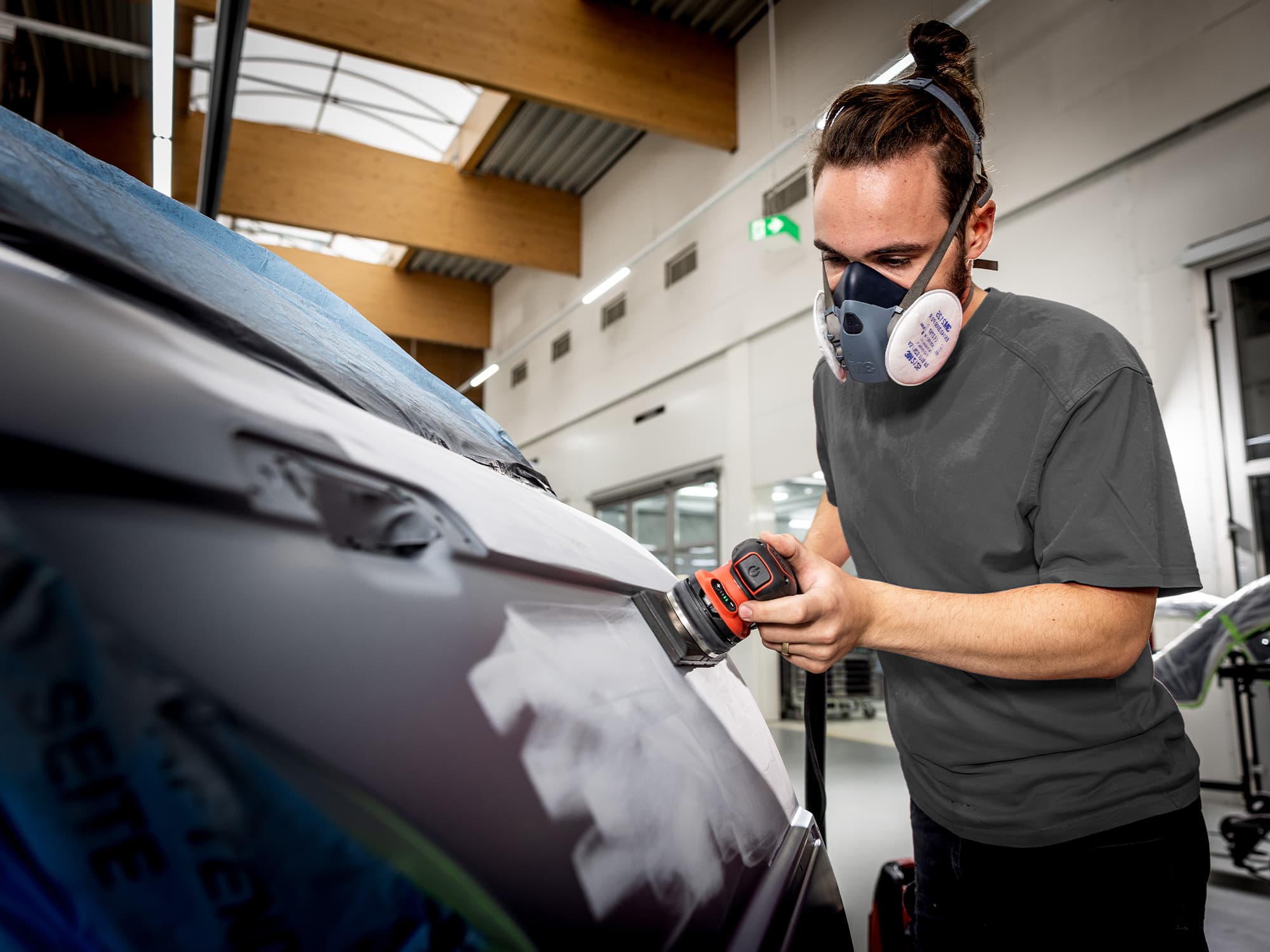 Un mecánico de carrocería lija la pintura de la puerta de un coche con la lijadora orbital de FLEX