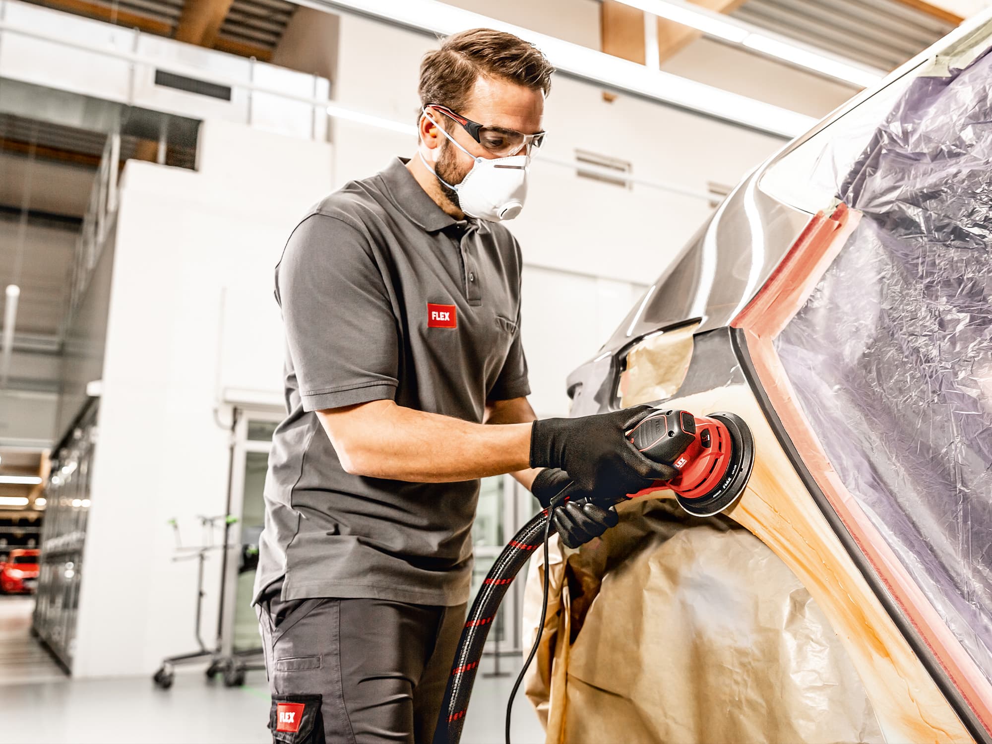 Un mecánico de carrocería lija la pintura de la puerta de un coche con la lijadora excéntrica de FLEX