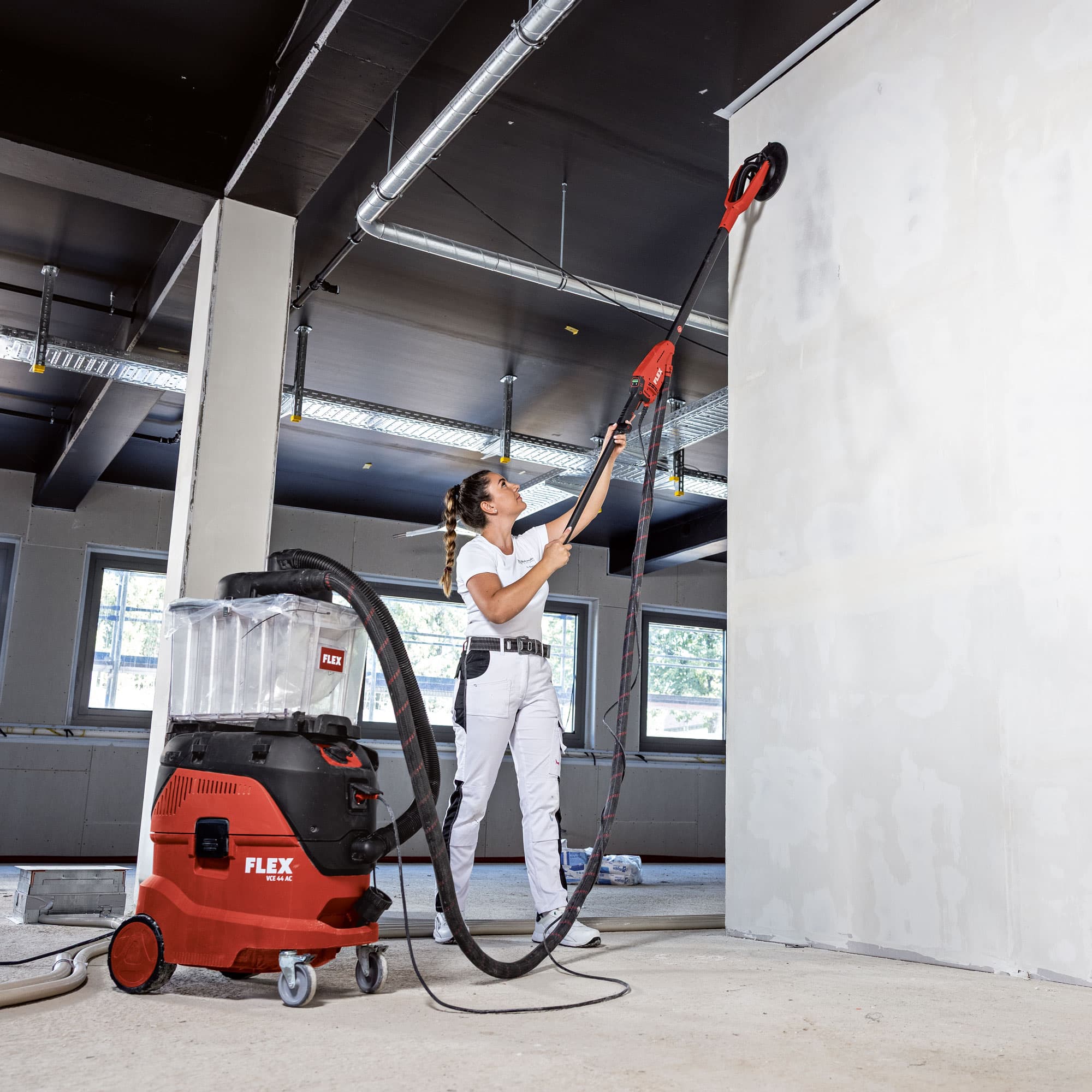 Malermeisterin Nina schleift mit dem FLEX Wand- und Deckenschleifer GE 6 X und Verlängerung eine hohe Decke, angeschlossen an einen FLEX Sicherheitssauger.